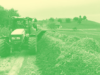 Traktor mit Kompostwender fährt Kompostmiete entlang.